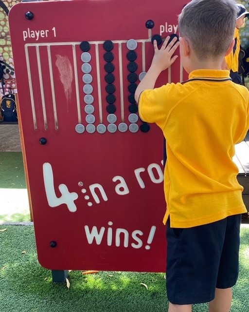 Young school boy playing with 4 in a row Sensory Panel in an outdoor playground