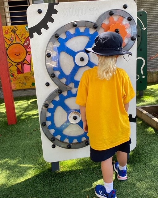 Young school student playing outdoors at school on a "Gears" sensory panel