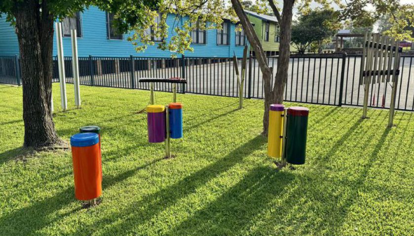 Outdoor musical instruments installed in a school playground on the grass under some trees
